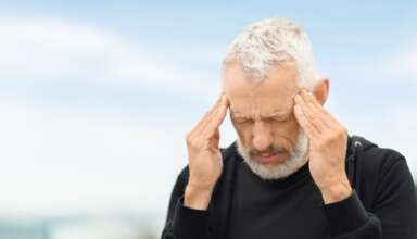Closeup of elderly sportsman feeling bad while exercising outdoor, touching his temples, senior man suffering from headache migraine during workout, running by street, copy space