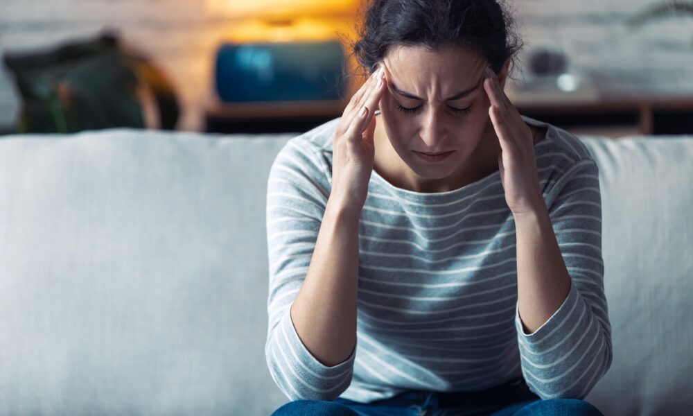 Young woman with headache sitting on the sofa in the living room